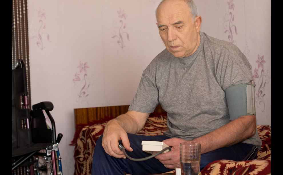 Ældre mand sidder på en seng og har en blodtryksmåler på armen